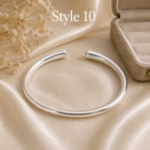 May include: A polished silver cuff bracelet with a smooth, rounded, open-ended design. The bracelet features a clean, minimalist aesthetic with rounded tips. The text 'Style 10' is visible in the upper portion of the image above the jewelry piece.