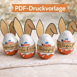 Può includere: Immagine pasquale con quattro ovetti Kinder Sorpresa decorati con orecchie di coniglio di carta. Le uova hanno involucri arancioni e bianchi con il logo Kinder e testo. Un coniglio bianco e uova decorate sullo sfondo.