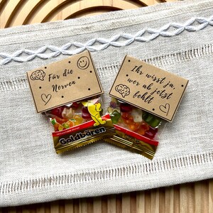 May include: Two small bags of Goldb&auml;ren gummy candies with brown paper toppers. One topper reads "F&uuml;r die Nerven" with a brain graphic, a heart, and a smiley face. The other reads "Ihr wisst ja, wer ab jetzt fehlt" with a brain graphic and a heart.