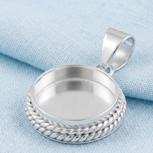 May include: A silver-toned circular pendant setting featuring a smooth, recessed center for a stone or cabochon, surrounded by a decorative twisted rope-style border and topped with a polished, integrated bail for necklace attachment.