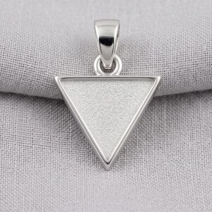 May include: A silver-toned triangular pendant featuring a textured, matte-finish center framed by a smooth, polished border. The pendant includes a sturdy, integrated bail at the top, designed for attachment to a chain or cord for wear as a necklace.