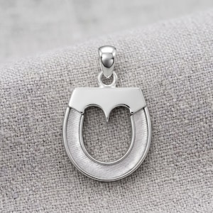 May include: A silver-toned horseshoe pendant featuring a polished smooth top section and a brushed, textured finish on the curved lower portion. The pendant includes a small, polished silver-toned bail at the top for attachment to a chain.