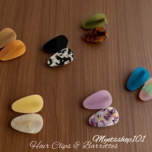 May include: A collection of colorful hair clips and barrettes in various shapes and patterns. The clips include solid colors like black, yellow, and blue, as well as patterned designs. The text "Hair Clips & Barrettes" and "Myetsshop101" are visible.
