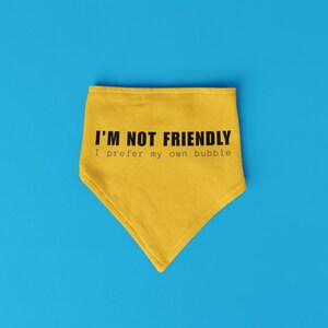 May include: Yellow bandana with the text "I'M NOT FRIENDLY I prefer my own bubble" in black. The bandana is triangular and set against a bright blue background. The text is centered on the bandana.