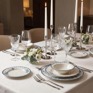 May include: Elegant table setting with white tablecloth, featuring floral-patterned plates, crystal glassware, and lit candles in silver holders. A small floral arrangement adds a touch of freshness. Ideal for a formal dinner or special occasion.
