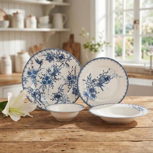 May include: A set of cream-colored ceramic dishes with blue floral and bird designs. The set includes large plates, smaller plates, and bowls. The rims of the plates and bowls are trimmed with a blue border. The dishes are arranged on a wooden surface.