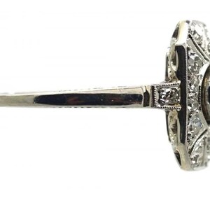 May include: A vintage-style ring with a silver band and a rectangular face. The face is adorned with multiple small diamonds and a larger, round diamond. The ring is set against a white background.