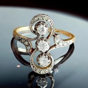 May include: A vintage gold ring with three diamonds, each surrounded by smaller stones. The ring has an elaborate, swirling design with a polished gold band and a silver setting for the diamonds. The ring's design is intricate.