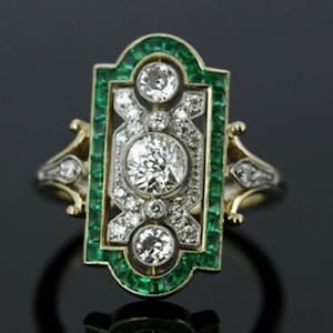 May include: An Art Deco ring with a central diamond and smaller diamonds, framed by an emerald border. The ring has gold detailing and a rectangular shape, showcasing a vintage design. The ring's design is reminiscent of the 1920s.