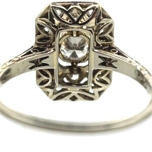 May include: A silver ring with an octagonal setting and a central, round, clear gemstone. The setting features intricate filigree and geometric designs. The band is thin and polished, with decorative elements near the setting.