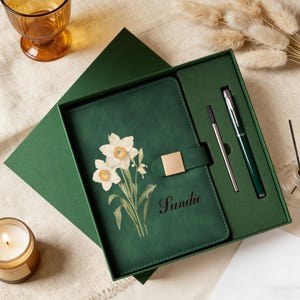 May include: A green journal with a floral design and the name "Sandie" in script, presented in a matching gift box with a pen and refill. The journal features a gold-colored clasp.