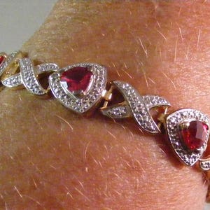 May include: A gold bracelet with a delicate design featuring alternating red heart-shaped gemstones and clear round stones.