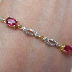 May include: A gold bracelet with a delicate design featuring alternating oval-shaped red gemstones and small clear stones.