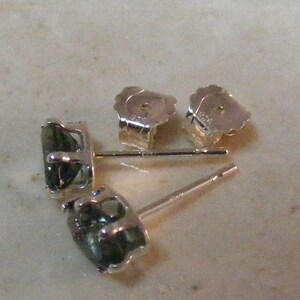 K&ouml;nnte beinhalten: Ein Paar silberne Ohrringe mit gr&uuml;nen Edelsteinen. Die Ohrringe sind im Stecker-Stil mit einem Stift und einem Schmetterlingsverschluss.