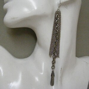 May include: Silver chain earrings with multiple strands and a long, pointed silver pendant.