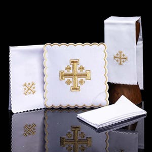 Può includere: Biancheria religiosa bianca con croci ricamate in oro. Il set include un cuscino quadrato, un panno piegato e due panni rettangolari con bordi smerlati. Le croci sono dettagliate con un design a quattro croci.