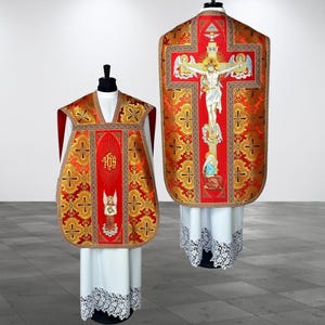 Può includere: Una casula liturgica rossa e oro con un intricato motivo damascato e croci. Il davanti mostra il monogramma IHS e un angelo, mentre il retro raffigura una dettagliata scena di crocifissione con una croce, angeli e figure religiose.