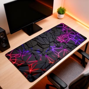 May include: A black rectangular mouse mat with a 3D geometric design. The design features a network of interconnected shapes with red, purple, and blue neon-style lines. The mouse mat is on a light wood desk.