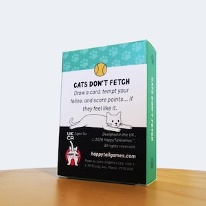 May include: A rectangular game box titled CATS DON'T FETCH with a teal top featuring paw prints, a yellow ball icon, and a white center panel. The text reads: Draw a card, tempt your feline, and score points... if they feel like it. Includes a cat illustration, the Happy Tail Games logo, and copyright information.