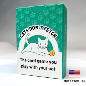 May include: A teal and white rectangular card game box titled Cats Don't Fetch. The box features a white cat illustration playing with a yellow ball, a repeating paw print pattern, and the text The card game you play with your cat.