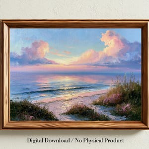 Può includere: Un dipinto paesaggistico incorniciato che raffigura un tramonto costiero con morbide nuvole rosa e blu sopra un oceano calmo. Il primo piano presenta dune sabbiose coperte di erba alta e piccoli fiori viola, con la luce che si riflette.