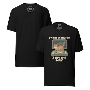 Pode incluir: T-shirt preta com um gato de desenho animado em um teclado de computador e o texto "I'M NOT IN THE WAY I AM THE WAY." A parte de trás da camisa tem um logotipo circular. A camisa é feita de um material macio.
