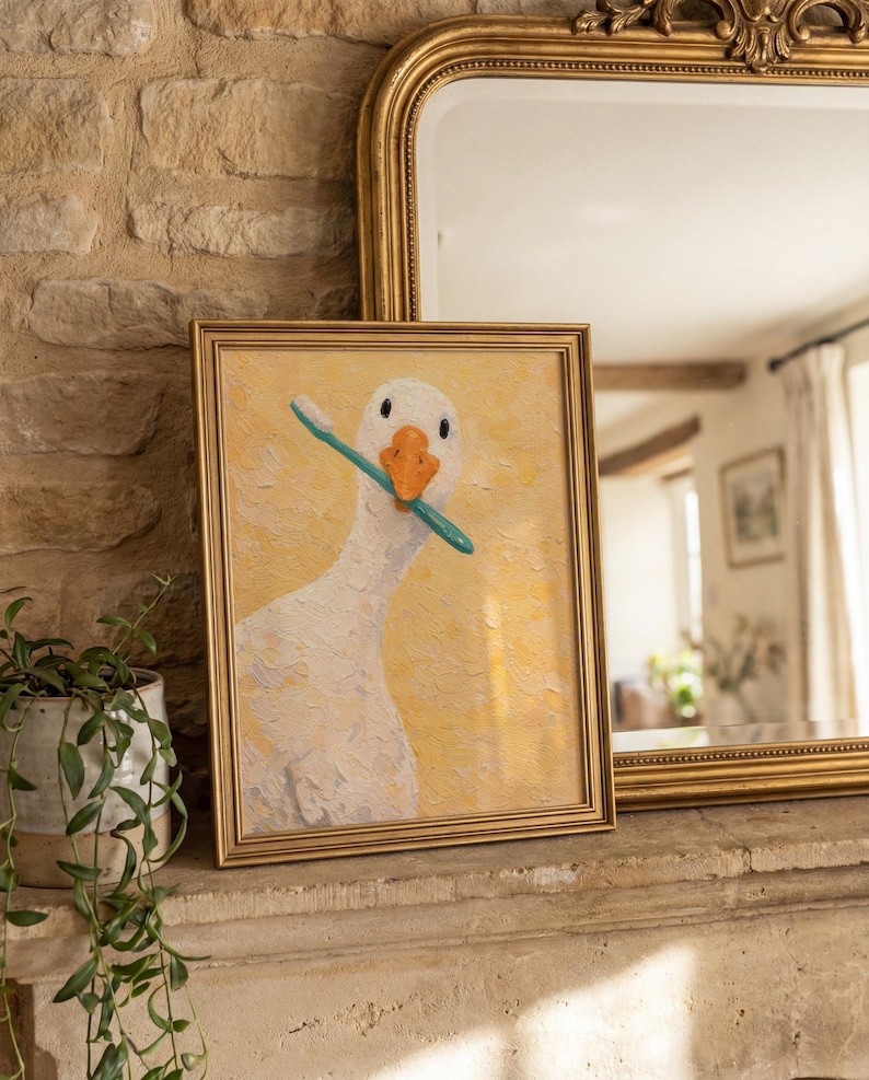 May include: A framed picture of a white goose with a blue toothbrush in its beak, set against a yellow backdrop. The artwork is in a gold frame. The picture is displayed on a stone surface.