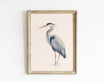 May include: A framed wall art print featuring a detailed illustration of a great blue heron standing in profile. The bird has grey and blue plumage, a long neck, and a sharp orange beak, set against a solid cream background within a wooden frame.