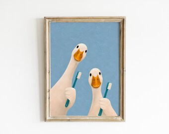 May include: A framed wall art print featuring two white geese with orange beaks against a textured light blue background. Each goose is holding a teal toothbrush with white bristles, positioned as if they are about to brush their beaks.