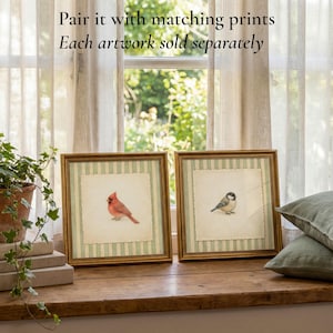 May include: Two framed bird prints with gold frames. One features a red cardinal, the other a small bird. The artwork is set against a striped background. The text on the image says, "Pair it with matching prints. Each artwork sold separately."