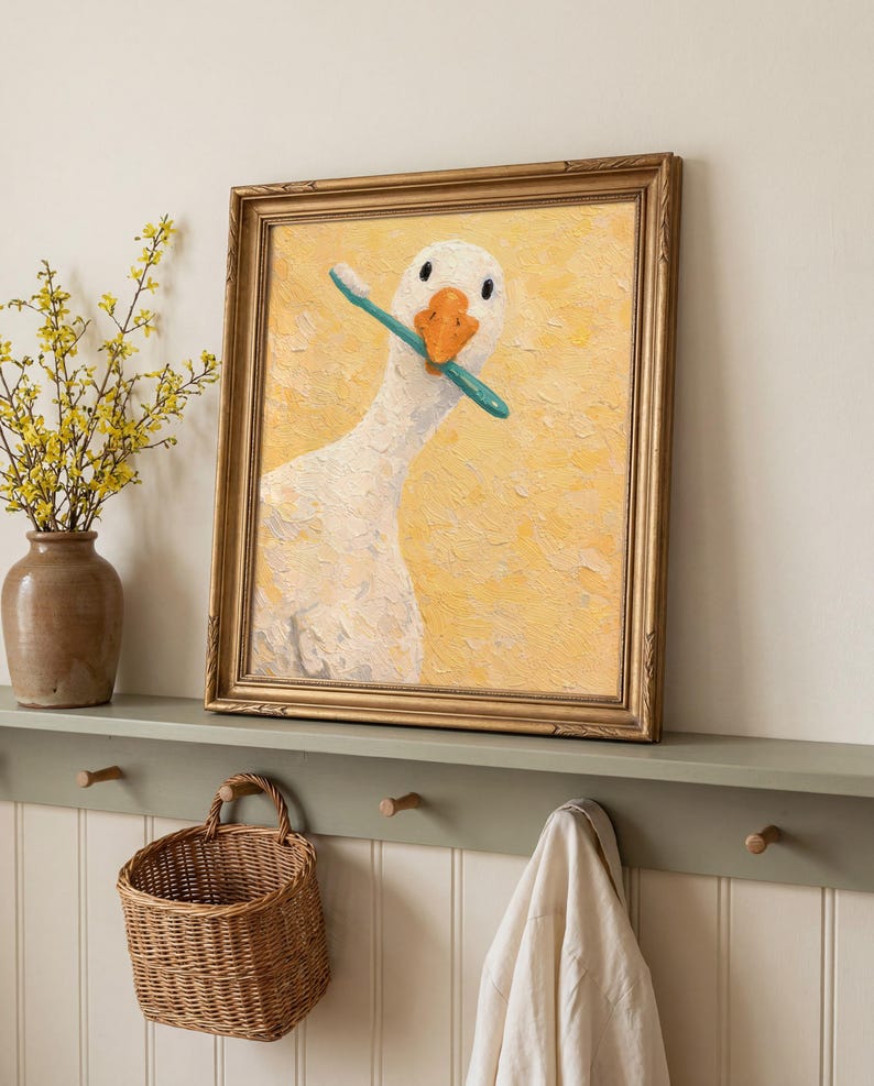 May include: A framed painting of a white goose with an orange beak, holding a blue toothbrush. The artwork is set against a textured yellow background and is enclosed in a gold-coloured frame. The painting is a humorous piece.