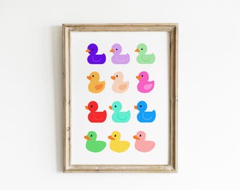 May include: A framed print featuring twelve colorful rubber duck illustrations. The ducks are arranged in three rows of four, each in a different bright color, including purple, green, and yellow. The frame is a light brown color.
