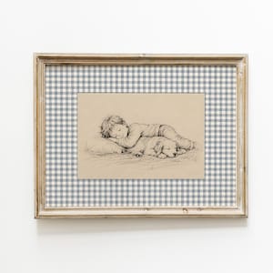Op de afbeelding: Een ingelijste houtskooltekening op beige papier met een vredig slapend kind dat het hoofd op een hond laat rusten. Het kunstwerk is voorzien van een passe-partout met een blauw-wit ruitpatroon en een lichtgekleurde houten lijst.