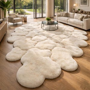 Könnte beinhalten: Ein großer, cremefarbener Teppich mit einer markanten, unregelmäßigen, wolkenartigen Form, die aus mehreren abgerundeten, plüschigen Segmenten besteht. Der Teppich hat eine dicke Hochflor-Textur, die den Boden bedeckt und weich wirkt.