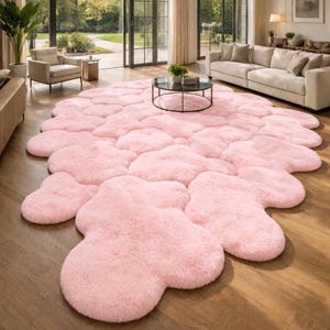 Op de afbeelding: Een grote, zachte, roze vloerkleed met een onregelmatige, wolkachtige vorm. Het kleed ligt op een houten vloer, en de kamer heeft grote ramen en meubels in neutrale tinten. Geschatte afmetingen: 200 cm x 300 cm.