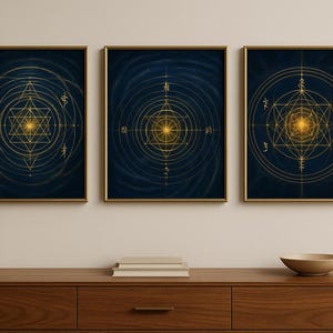 Puede incluir: Tres impresiones artísticas enmarcadas con diseños geométricos dorados sobre un fondo azul oscuro. La obra de arte presenta intrincados patrones de líneas, círculos y símbolos, con una luz dorada central. Los marcos son dorados y la obra se exhibe sobre un mueble de madera.