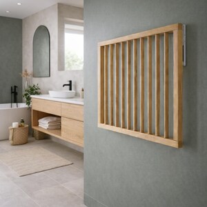 Könnte beinhalten: Ein rechteckiger, an der Wand montierter Handtuchhalter aus hellem Holz mit vertikalen Lamellen. Der Halter ist an einer grauen Wand befestigt. Das Badezimmer umfasst ein Waschbecken, einen Spiegel und eine Badewanne.