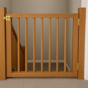 Puede incluir: Una barrera de escalera de madera con barrotes verticales y una puerta con bisagras. La barrera es de madera de color claro y tiene herrajes de color latón. Está instalada en la parte superior de una escalera.