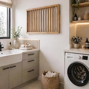 Könnte beinhalten: Ein modernes Waschzimmer in neutralen Tönen. Es verfügt über eine weiße Waschmaschine, eine Wanddekoration mit hellen Holzlamellen und einen Weidenkorb. Der Raum hat auch ein Waschbecken, Schränke und einen Teppich, wodurch ein funktionaler und stilvoller Raum entsteht.