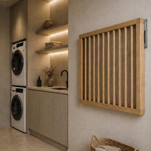 Könnte beinhalten: Ein an der Wand montierter Trockenständer aus hellem Holz mit vertikalen Stäben. Der Ständer ist an einer neutralfarbenen Wand in einem Waschraum angebracht. Eine gestapelte Waschmaschine und ein Trockner sind im Hintergrund zu sehen.