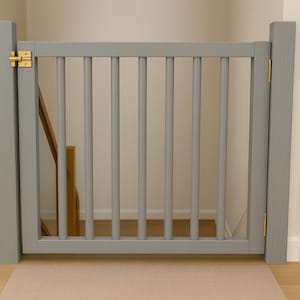 May include: A grey wooden safety gate with vertical spindles and brass hinges. The gate is installed in a doorway or opening, with a light-coloured rug beneath it. The gate is designed to prevent access to a staircase.
