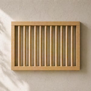 Könnte beinhalten: Ein rechteckiger Holzrahmen mit vertikalen Dübeln. Der Rahmen und die Dübel sind in einem hellen, natürlichen Holzton gehalten. Das Design ist schlicht und minimalistisch, passend für verschiedene Einrichtungsstile. Der Hintergrund ist eine neutrale, strukturierte Wand.