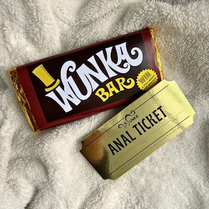 May include: A Wonka Bar chocolate bar with gold foil wrapping and a gold ticket that reads "Anal Ticket". The candy bar is brown with white and yellow text. The ticket is gold with black text.