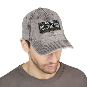 May include: A gray, distressed baseball cap featuring a black and gold patch with the text "AUDI AU 1932" in white. The cap has a curved brim and a faded, vintage look, suitable for car enthusiasts.