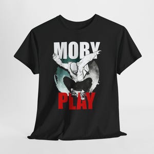 Puede incluir: Camiseta negra con un gráfico de una persona en el aire, con las palabras "MOBY" arriba y "PLAY" abajo. El gráfico es blanco y rojo, sobre un fondo turquesa y gris.