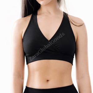 May include: Black halter-style sports bra with a V-neck design. The bra features a wrap-style front and a supportive band under the bust. The text "ZaraGlobalGoods" is printed on the front. The bra is made of a smooth, solid black fabric.