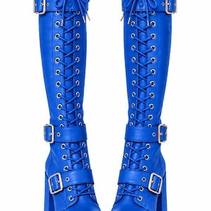 May include: A pair of vibrant blue knee-high boots featuring a lace-up front with silver-toned eyelets, three adjustable straps with gold-toned buckles, a thick platform sole, and a chunky block heel. The boots have a smooth finish throughout.