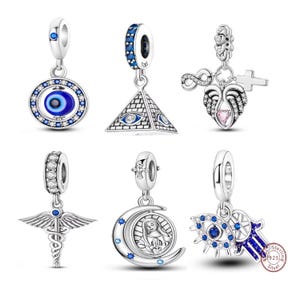 May include: A collection of silver charms with various designs. Charms include an evil eye, a pyramid with an eye, an infinity symbol with wings and a cross, a medical symbol, a crescent moon with a religious figure, and a Hamsa hand.