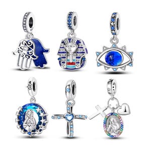 May include: A collection of silver-toned charm pendants with various designs. The charms include a blue Hamsa hand, a pharaoh, an eye, a religious figure, a cross, and a cross with a heart. Each charm has a loop for attaching to a bracelet or necklace.