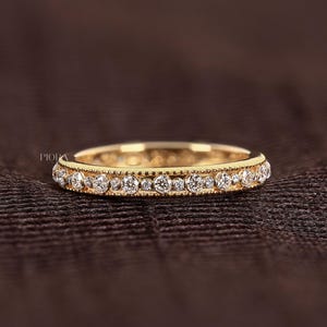 May include: A yellow gold eternity band featuring a continuous row of round brilliant cut diamonds set within a milgrain detailed channel. The ring displays the text PIORA on the left side and a small logo in the bottom right corner.